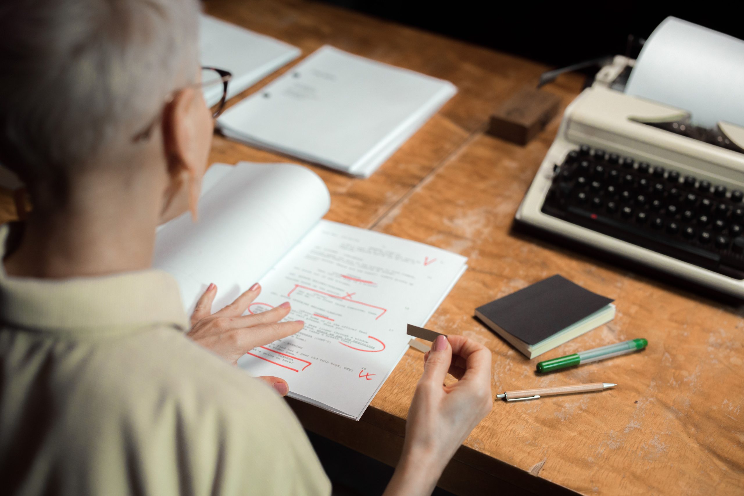 Writer reviewing a marked manuscript beside a typewriter, representing the editorial stage of book creation.